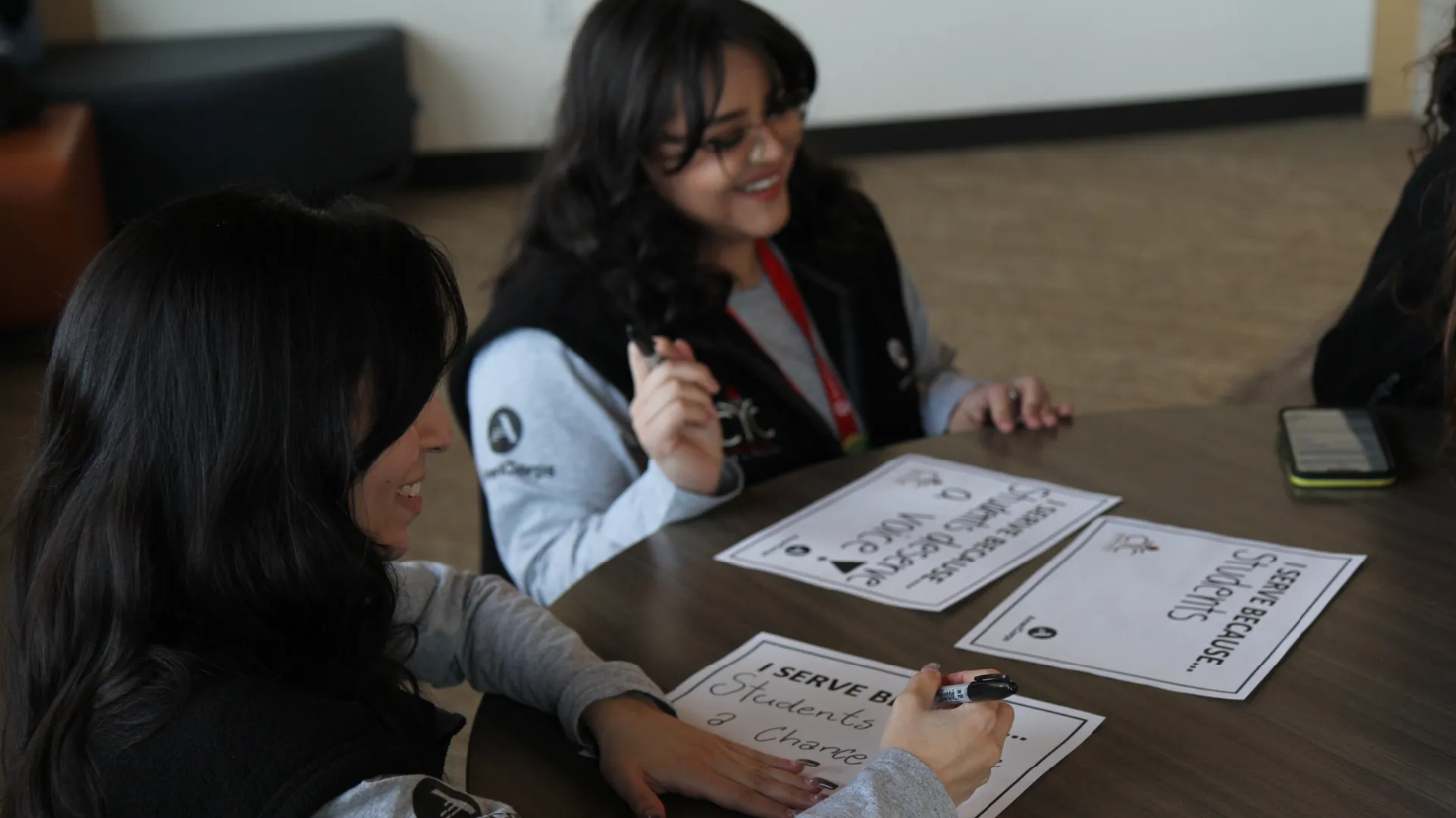 group of young people filling out signs that read "I serve because..."