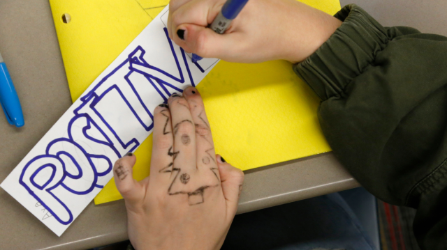 Hands with marker drawings on them, creating a sign that reads "POSITIVE"