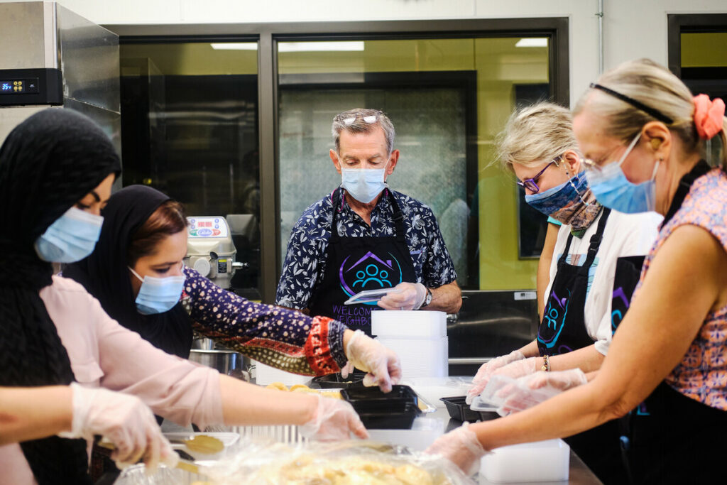 Group of masked people putting food in plastic containers